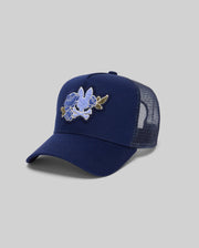 The KIDS AUGUSTE TRUCKER CAP (KO1500022) by Psycho Bunny is a navy blue mesh hat with a curved brim, embroidered bird and blue flowers chenille patch on front, adjustable snapback, shown on a plain gray background.