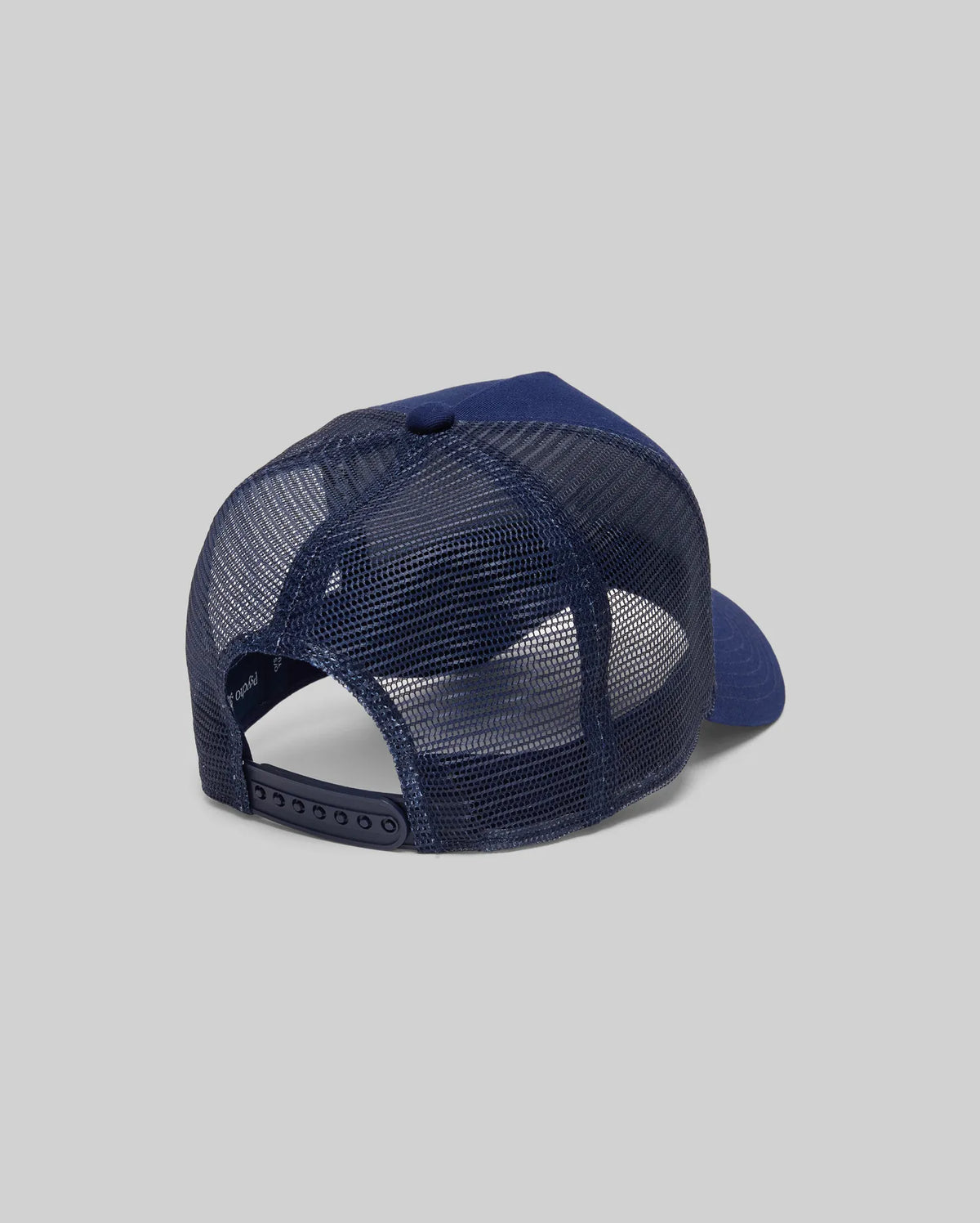The Psycho Bunny KIDS AUGUSTE TRUCKER CAP (KO1500022) in navy blue is shown from the back, featuring an adjustable snapback and curved brim, set against a plain gray background for a classic, comfortable fit.
