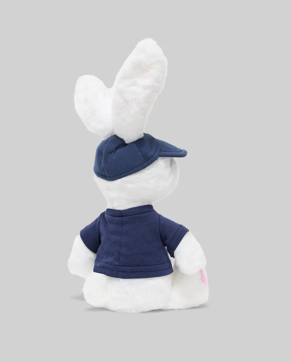 The PSYCHO BUNNY PLUSH - KO1700001 by Psycho Bunny is an ultra-soft bunny wearing a blue cap and shirt, shown from the back against a plain gray background.