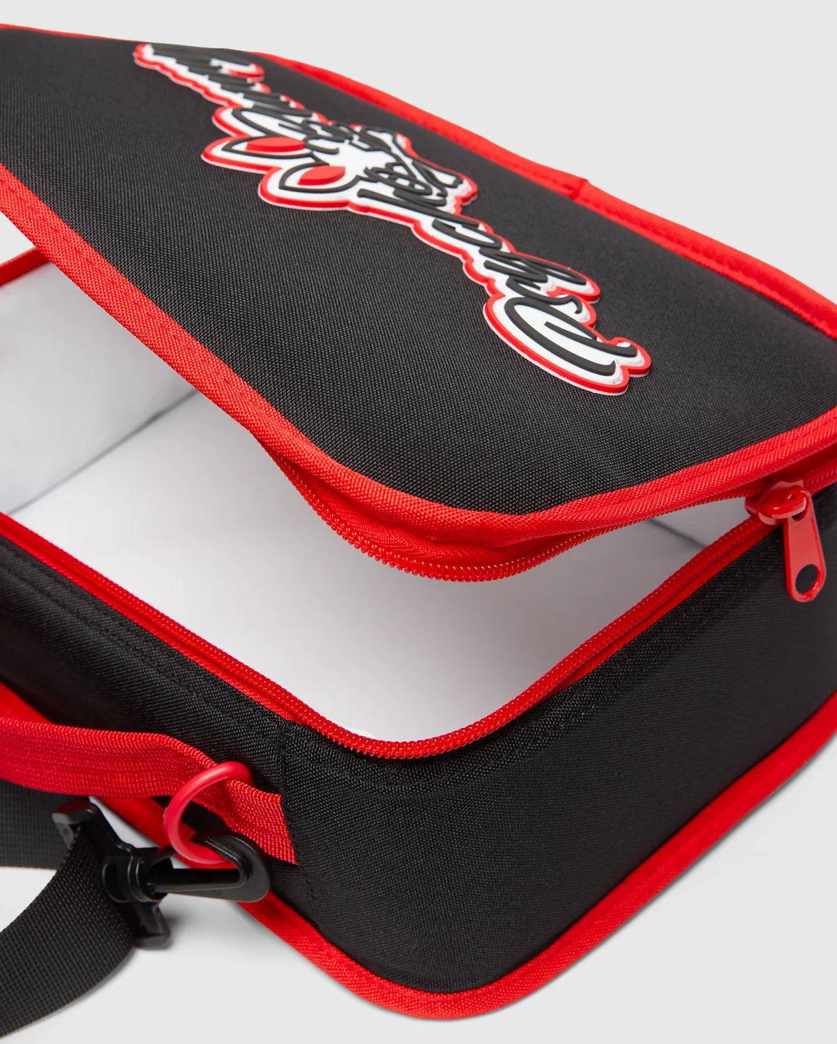 Black Kids Pal Lunch Box with red piping and zipper, featuring a large 3D white and red Psycho Bunny logo on the top, and an adjustable black strap. (2)