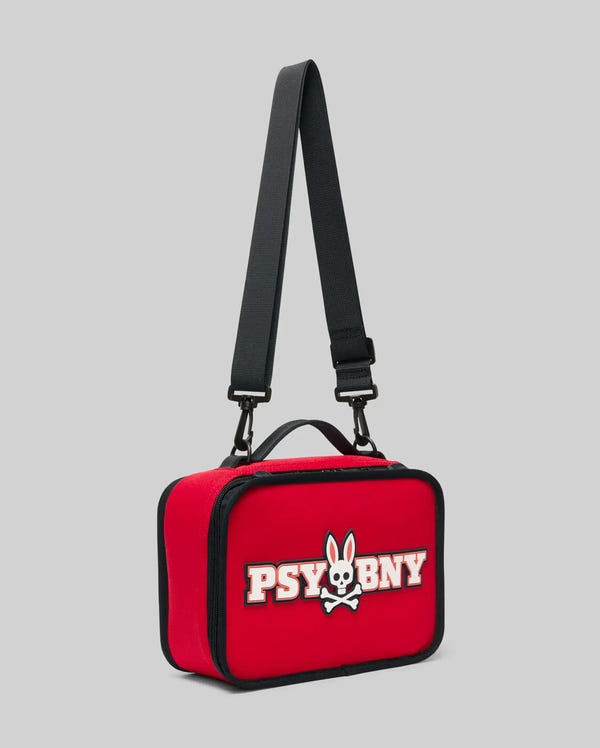 The PSYCHO BUNNY LUNCH BOX - KO2400002 by Psycho Bunny is a red insulated lunch box with a black adjustable strap and handle, featuring a white and black silicone "PSYBNY" bunny skull and crossbones on a light gray background.