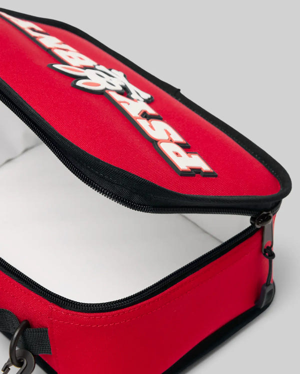 Close-up of the PSYCHO BUNNY LUNCH BOX - KO2400002 by Psycho Bunny, a red rectangular insulated bag with black edges, partially open to show its white interior. The top flap displays bold "RSX" text in black and white.