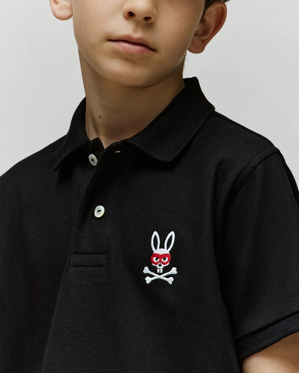 A child wearing a Psycho Bunny KIDS MISCHIEF BUNNY PIQUE POLO, made from soft Pima cotton with mother of pearl buttons and an embroidered bunny (red eyes, skull and crossbones) on the chest.