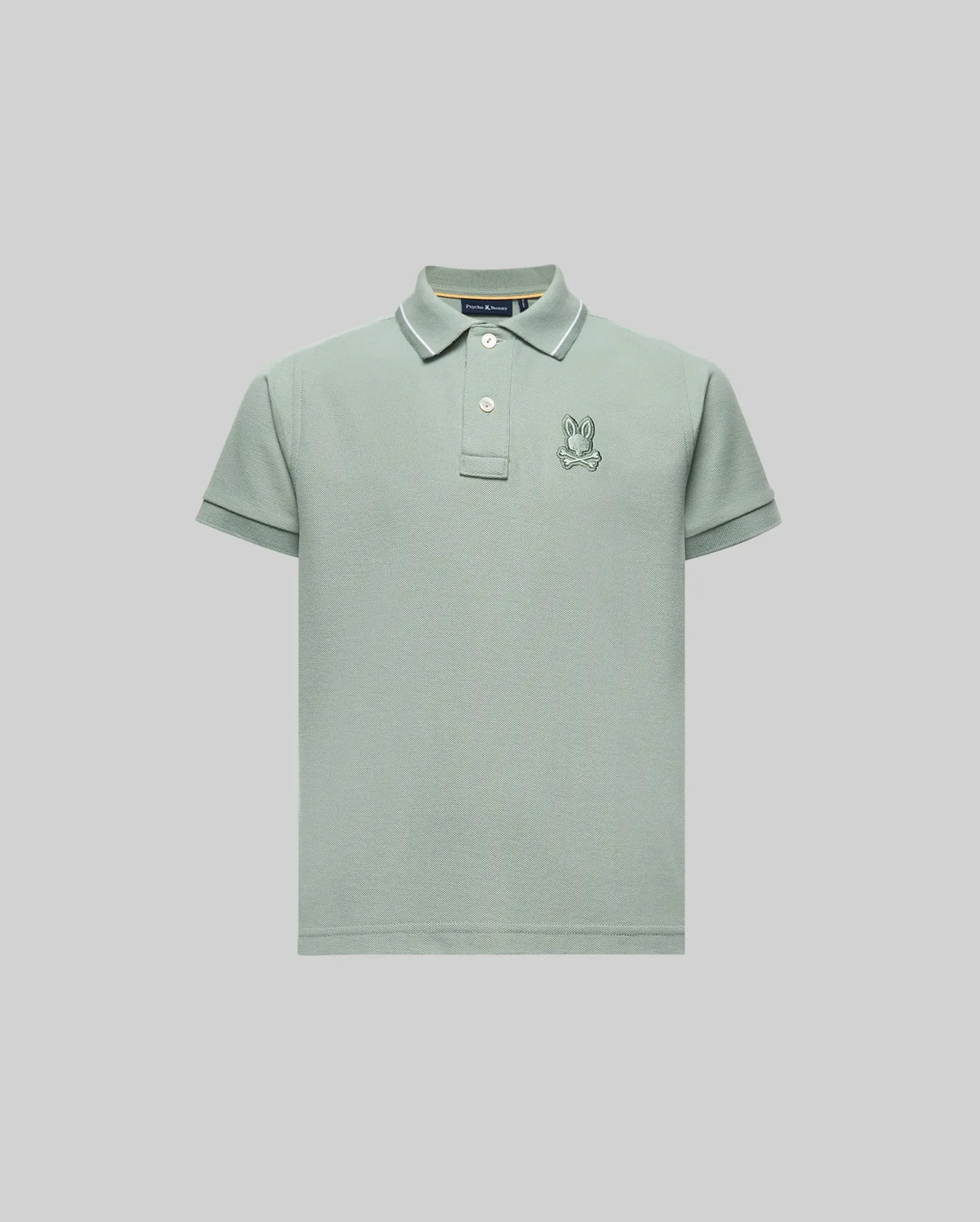 The Psycho Bunny KIDS FENLEY PIQUE POLO (KT0100023) features a light green color, regular fit, soft Pima cotton, short sleeves, collar, button placket, and an embroidered cartoon rabbit logo on the left chest. Shown on a light gray background.