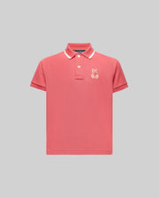 The KIDS FENLEY PIQUE POLO - KT0100023 by Psycho Bunny is a pink short-sleeve polo with a white collar stripe, three buttons, and an embroidered bunny logo on the left chest, made from soft Pima cotton and shown on a plain gray background.
