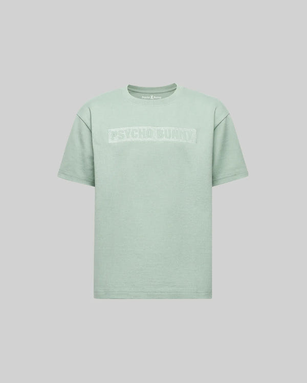 The KIDS ZAYN OVERSIZED GRAPHIC TEE (KT0200001) by Psycho Bunny is a light green, relaxed-fit kids' short-sleeve shirt with bold white "PSYCHO BUNNY" lettering on the chest, shown against a plain light gray background.