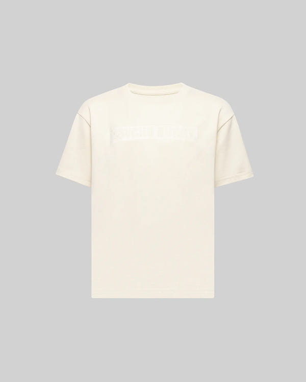 The KIDS ZAYN OVERSIZED GRAPHIC TEE (KT0200001) by Psycho Bunny is a heavyweight, off-white short-sleeve t-shirt with a subtle rectangular graphic across the chest, shown on a light gray background.