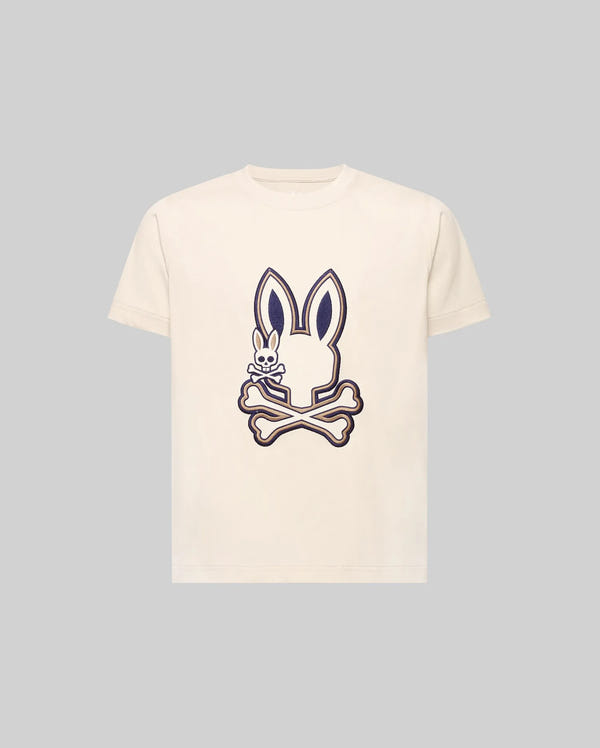 The Psycho Bunny KIDS WADE GRAPHIC TEE (KT0200054) is a cream-colored 100% cotton shirt featuring a large outlined bunny head above crossed bones and a small embroidered bunny holding a bone on the front.