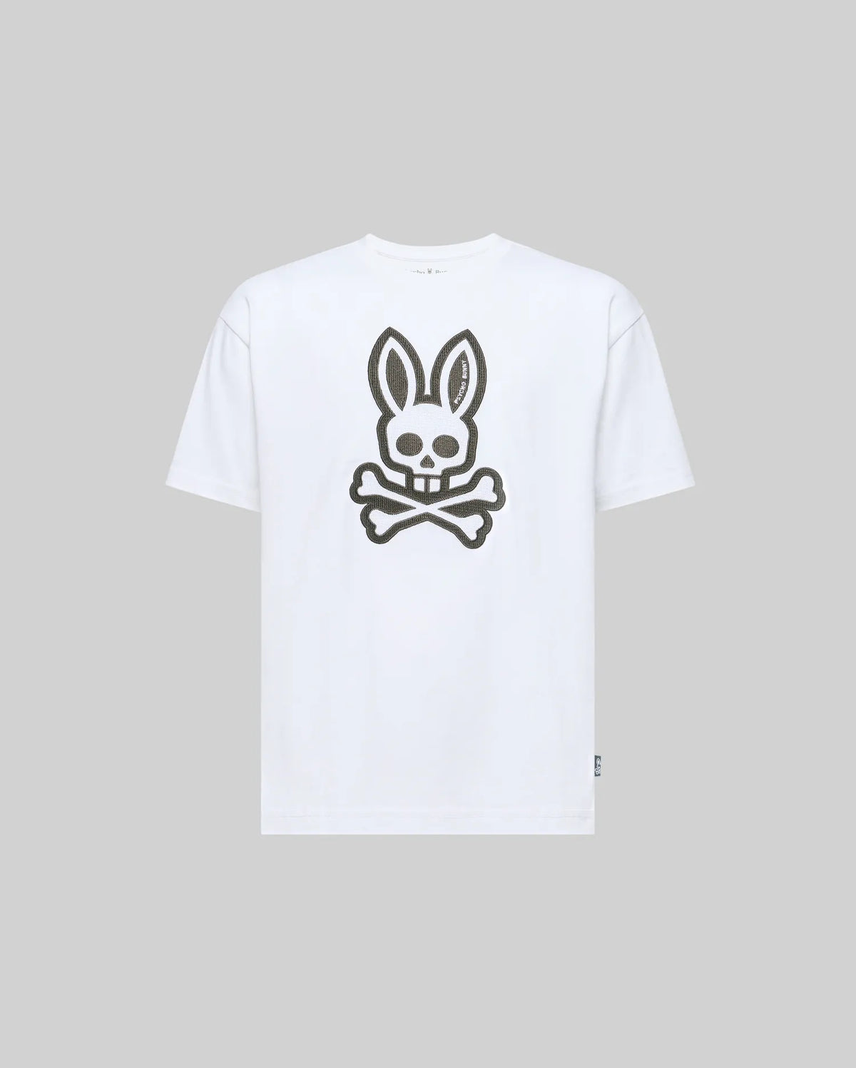 The Psycho Bunny KIDS RYDER OVERSIZED TEE (KT0200056) is a white premium Pima cotton tee, featuring an oversized graphic of a skull with bunny ears above crossed bones on the front, shown on a light grey background.