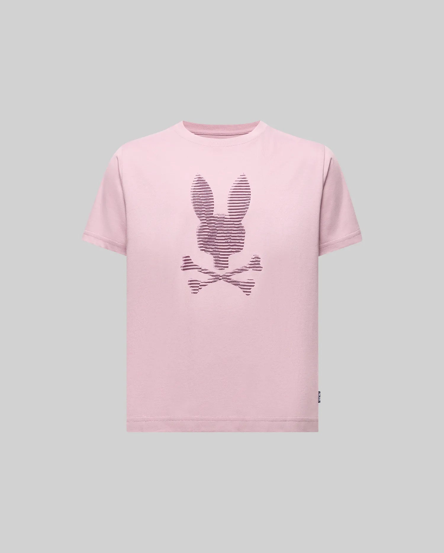 The Psycho Bunny KIDS GRANT BUNNY GRAPHIC TEE (KT0200061) is a light pink tee with a bunny head and crossed bones in horizontal lines on the chest, made from soft Pima cotton on a solid gray background. Made in Peru.