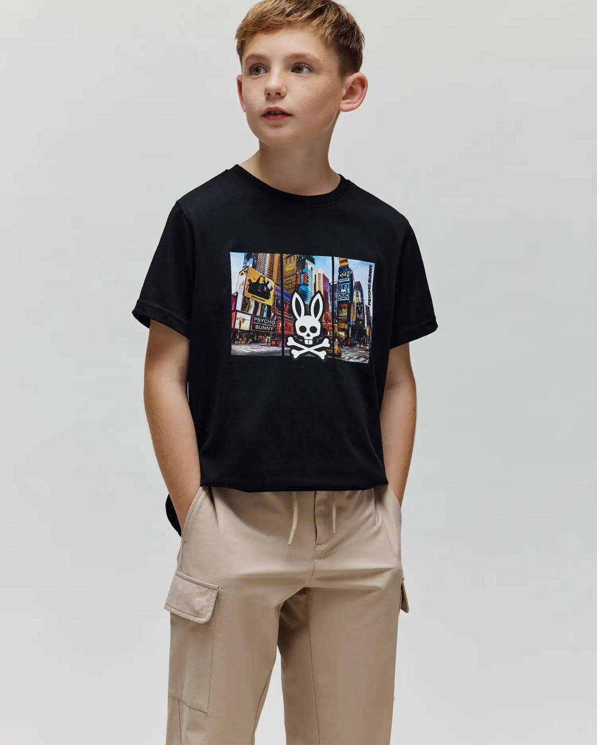 Kids Zeke Graphic Tee, black jersey t-shirt with a classic fit, featuring a large colorful Times Square graphic print on the chest, centered with the iconic white Psycho Bunny skull and crossbones logo.
