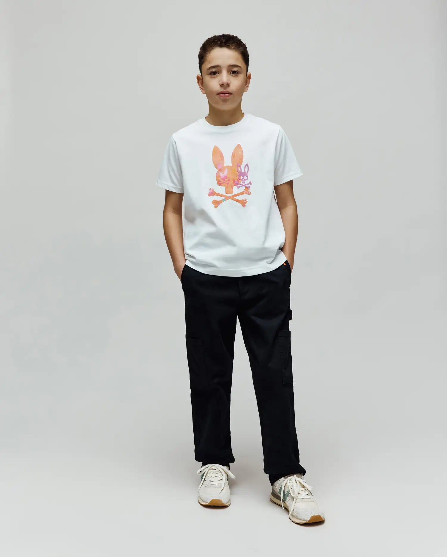 White Kids Van Graphic Tee, a classic fit jersey knit t-shirt featuring a large, colorful watercolor-style Psycho Bunny skull and crossbones graphic on the center chest, paired with black utility pants.
