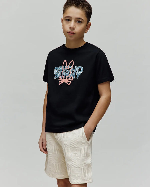 Kids Herman Graphic Tee, a black classic fit jersey t-shirt with a large pixelated pink and blue embroidered Psycho Bunny logo on the chest, paired with cream textured knit shorts featuring an all-over subtle bunny skull pattern.