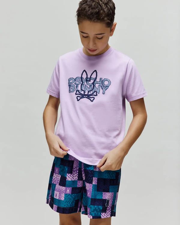 Kids Herman Graphic Tee, a lavender jersey t-shirt with a classic fit, showcasing a large, pixelated blue and purple Psycho Bunny skull and crossbones logo prominently on the chest.