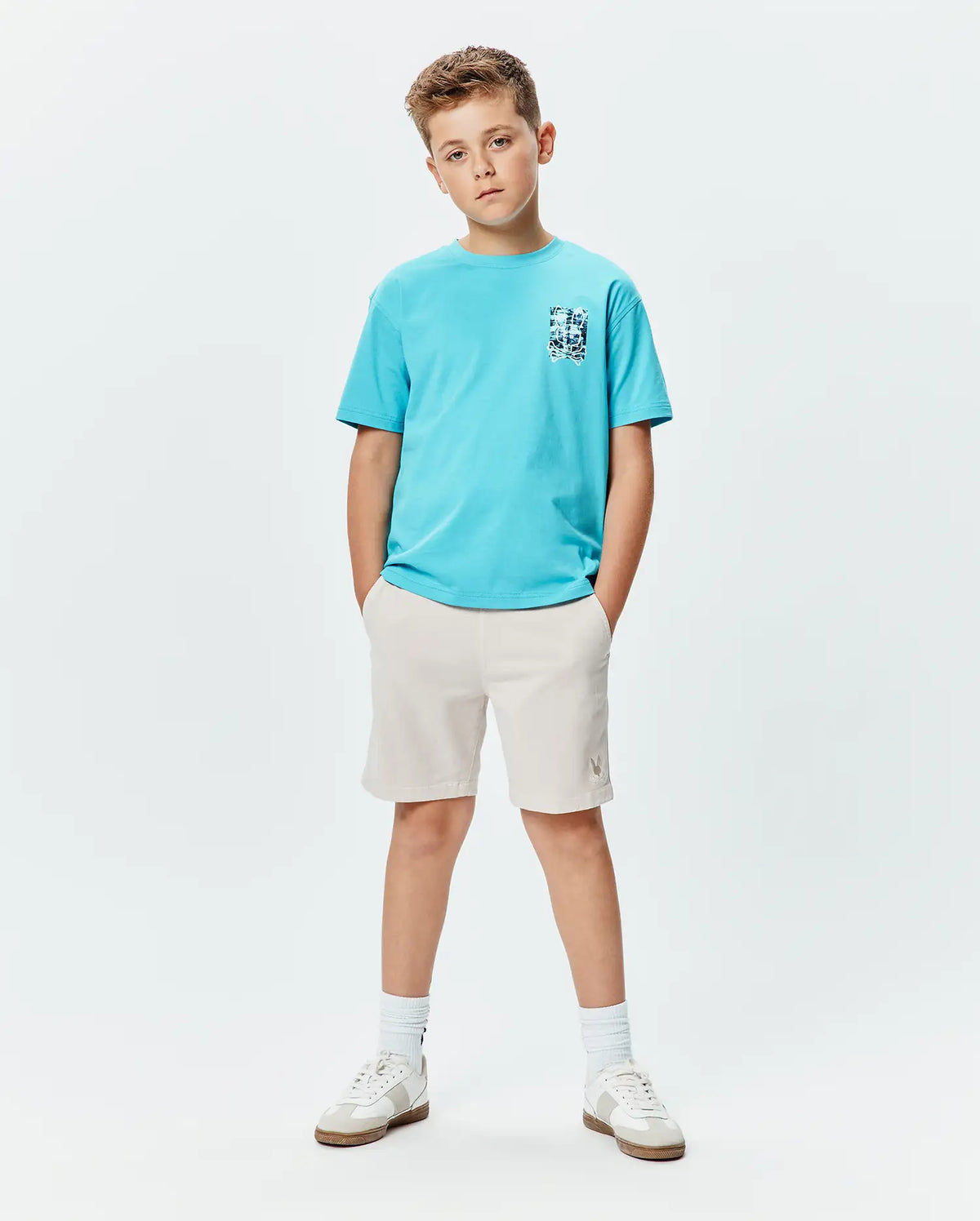 Kids Isaac Relaxed Fit Tee in bright blue jersey with a blue and white abstract bunny skull chest graphic, paired with light beige shorts featuring a small embroidered Psycho Bunny logo on the left thigh. (4)