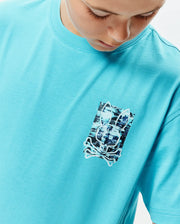 Kids Isaac Relaxed Fit Tee in vibrant turquoise jersey, featuring a relaxed fit and a distressed, pixelated Psycho Bunny skull graphic print on the left chest with black, white, and blue accents. (3)