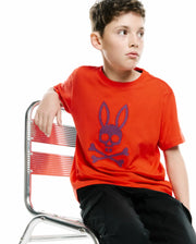 KIDS STAN GRAPHIC TEE in vibrant orange jersey, featuring a large central chest graphic of the iconic Psycho Bunny skull and crossbones logo in blue and purple patterned fill, offering a relaxed fit. (2)