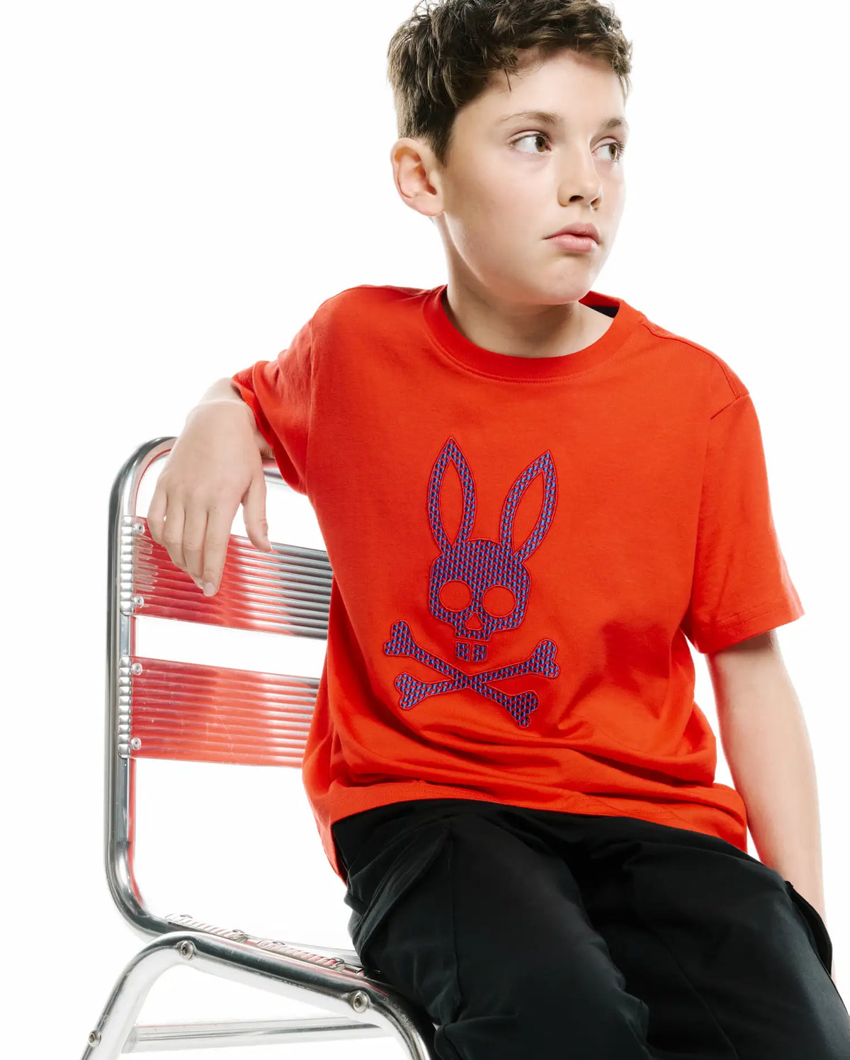 KIDS STAN GRAPHIC TEE in vibrant orange jersey, featuring a large central chest graphic of the iconic Psycho Bunny skull and crossbones logo in blue and purple patterned fill, offering a relaxed fit. (2)