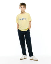Kids Jaydon Wordmark Graphic Tee, a pale yellow classic fit jersey t-shirt with a medium blue embroidered Psycho Bunny wordmark logo on the center chest, styled with navy cargo pants. (4)
