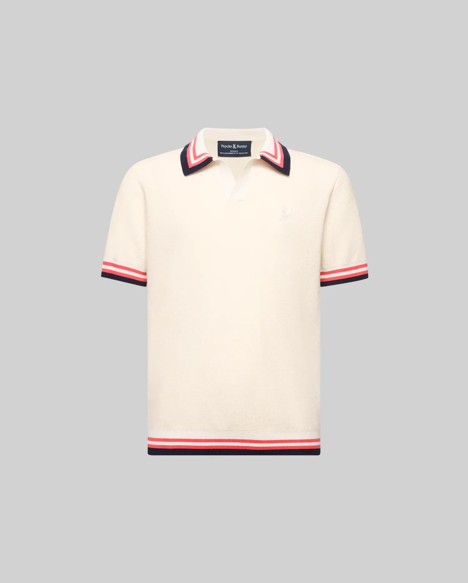 The Psycho Bunny KIDS CARTER KNIT POLO SHIRT (KT0400006) is a cream, short-sleeved 100% cotton polo with a Johnny collar and red, white, and navy stripes on the collar, cuffs, and hem, shown on a plain gray background.