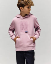A young boy with curly hair wears the Psycho Bunny KIDS GRANT HOODIE - KT0500020 in light purple, featuring an embroidered bunny and crossbones. He stands with hands in the front pocket, looking right against a plain background.