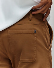 A close-up of a person wearing Psycho Bunny MENS RUSSELL CARPENTER PANT - MB0600005 in regular fit with a white shirt tucked in. Their hand, adorned with a silver ring, rests near the back pocket by the hammer loop.
