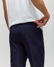 A man in a white shirt and PSYCHO BUNNY MENS BEN TECH JOGGER PULL ON pants (MB0600013) made from woven fabric stands with his back to the camera, pulling his shirt to show the "Psycho Bunny" logo above the back pocket.