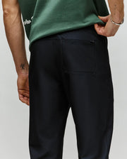 A person wearing a green t-shirt and dark "MENS BEN TECH JOGGER PULL ON - MB0600013" pants is shown from the back, one hand on their hip, with a back pocket featuring the Psycho Bunny brand name above it.