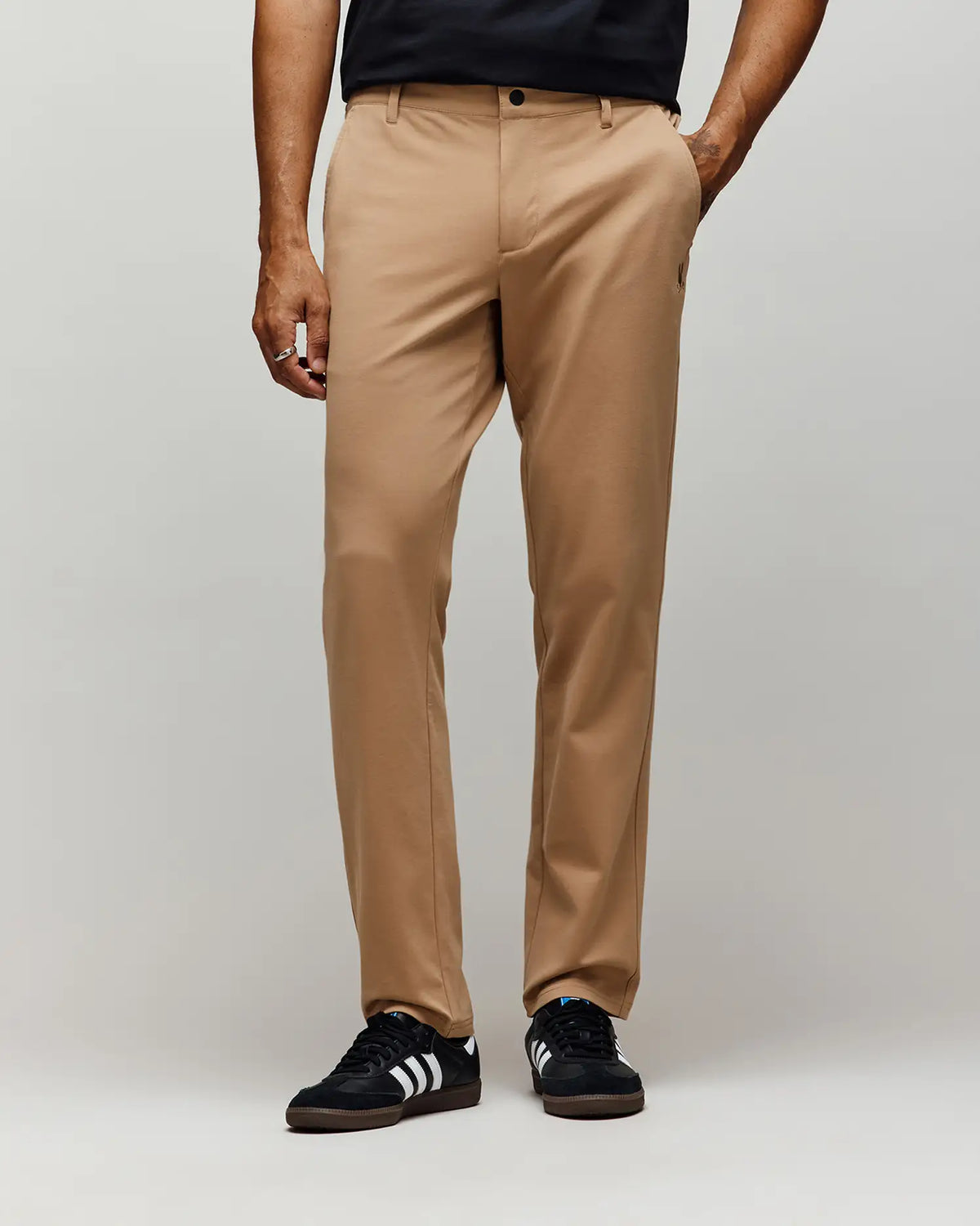 A person wearing Psycho Bunny MENS EDWARD PANT - MB0600014 in tan stands against a plain gray background; their upper body is partially visible.