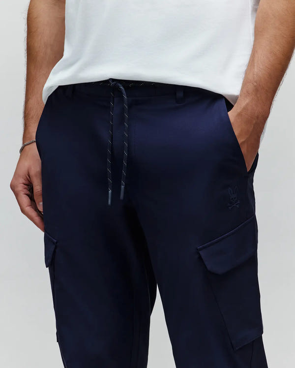 MENS LUKA CARGO PANT in navy blue, featuring a relaxed fit, smooth fabric, drawstring waist with white flecks, side cargo pockets, and a small tonal embroidered Psycho Bunny skull logo.