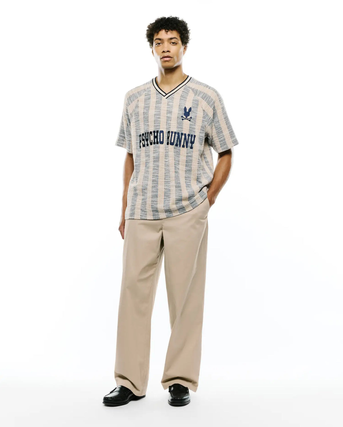 Textured beige and blue vertical striped knit V-neck shirt with black trim, featuring large PSYCHO BUNNY text and small skull logo on chest, paired with relaxed fit khaki Mens Aidan Chino Pant. (4)