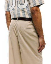 MENS Aidan Chino Pant in classic beige twill, featuring a relaxed fit and subtle PSYCHOBUNNY embroidery above the back pocket, paired with a textured beige and navy striped shirt with a large white graphic. (3)