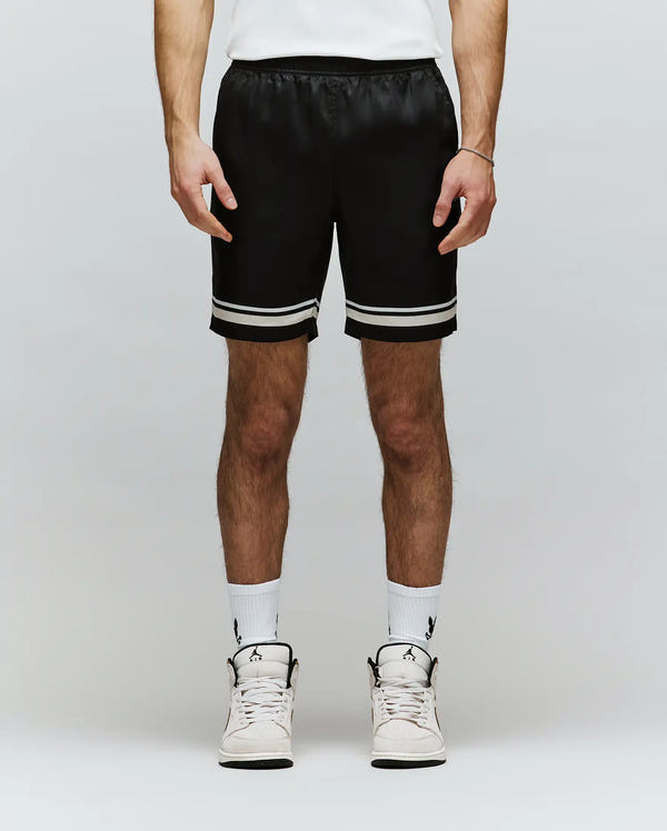 A person in Psycho Bunny MENS ADEN TENCEL SHORT - MB0700005, black with white stripes and made from 100% tencel, pairs them with white crew socks and high-top sneakers against a light background—effortless sustainable style.