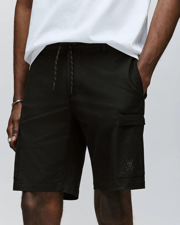 A person wears Psycho Bunny MENS ARLO CARGO SHORT - MB0700007, crafted from a premium cotton blend with a drawstring waist, zippered cargo pocket, and bunny logo near the hem; only the lower torso and upper legs are shown.