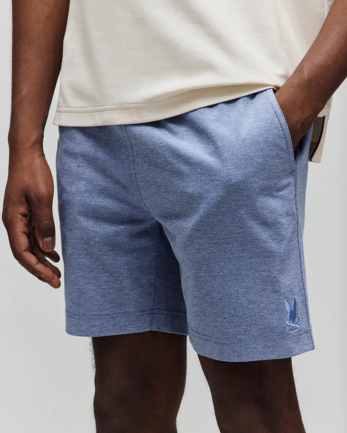 Mens Koda Oxford Short, heathered blue with a textured oxford weave, featuring a small, tonal embroidered Psycho Bunny skull logo on the lower left leg for a classic fit.