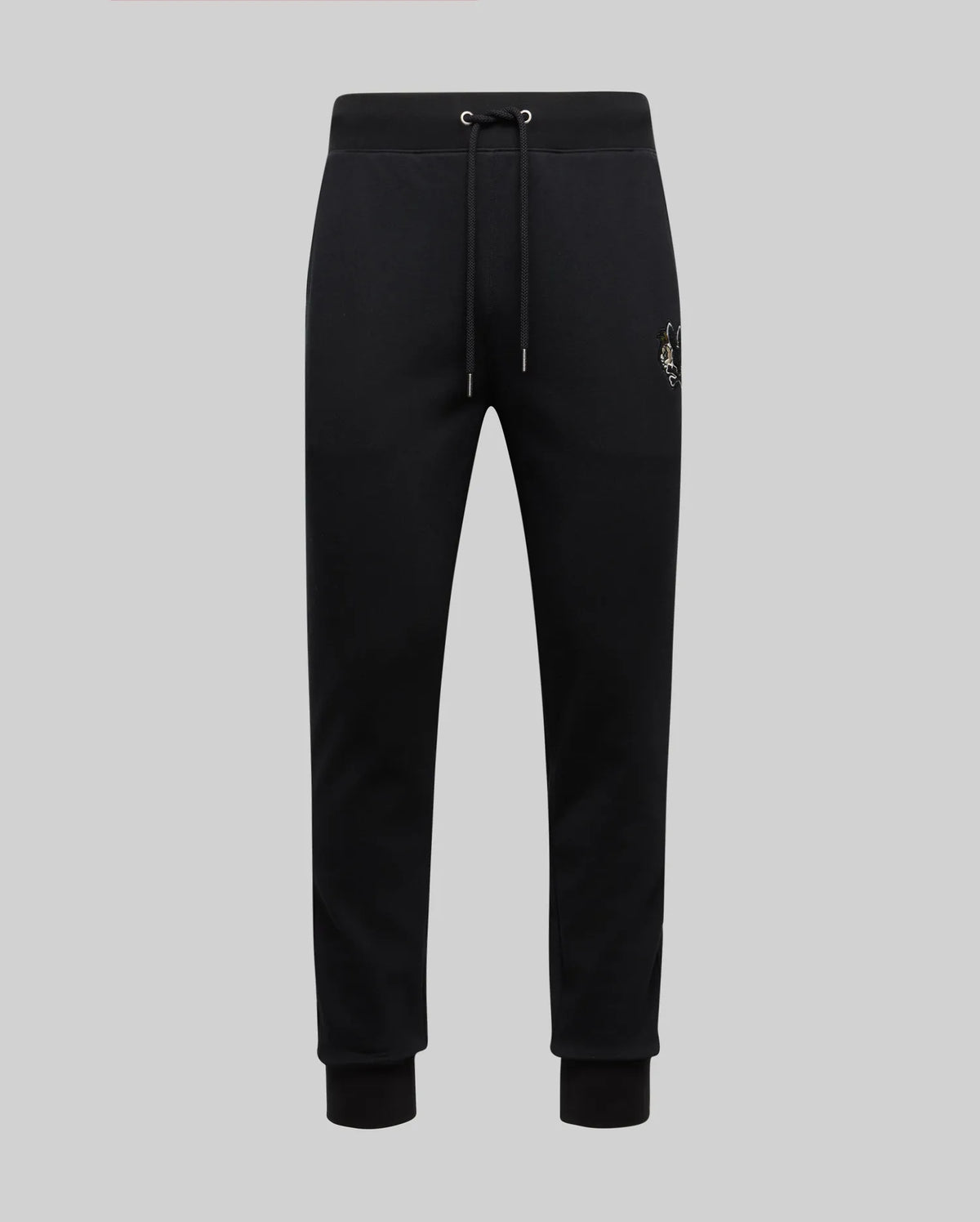 The Psycho Bunny MENS AUGUSTE JOGGER - MB0800015 in black features 100% cotton, an elastic waistband with drawstring, cuffed ankles, and a subtle chenille patch emblem on the left thigh, shown on a light gray background.