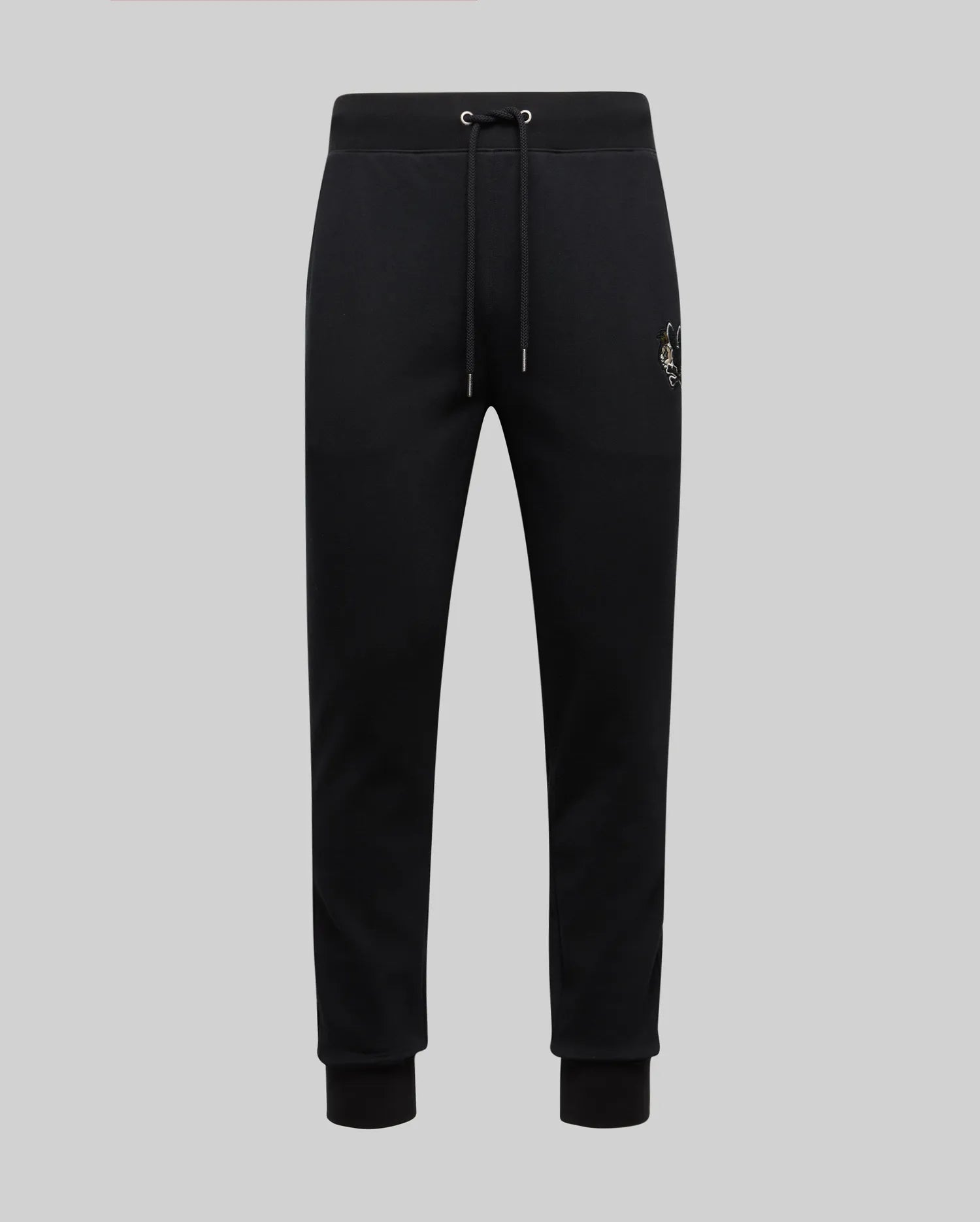 The Psycho Bunny MENS AUGUSTE JOGGER - MB0800015 in black features 100% cotton, an elastic waistband with drawstring, cuffed ankles, and a subtle chenille patch emblem on the left thigh, shown on a light gray background.