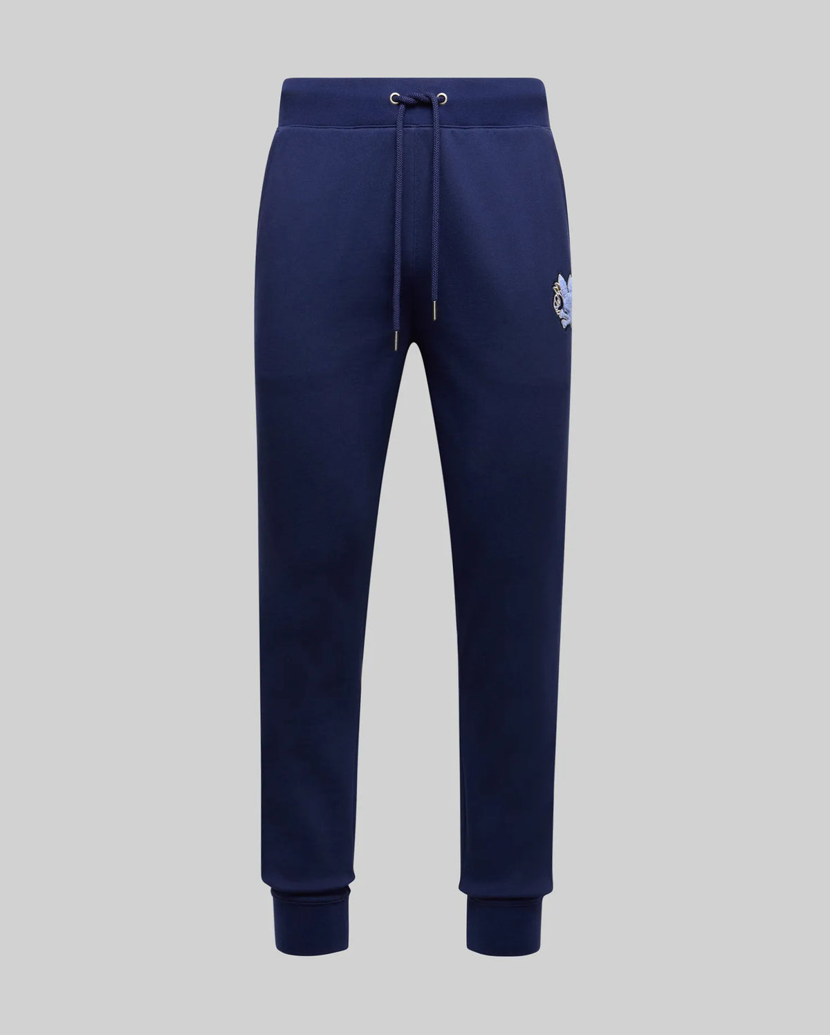 The Psycho Bunny MENS AUGUSTE JOGGER - MB0800015 in navy blue is crafted from 100% cotton with a drawstring waist, side pockets, ribbed cuffs, and a small embroidered tiger logo on the left hip, shown on a plain light grey background.