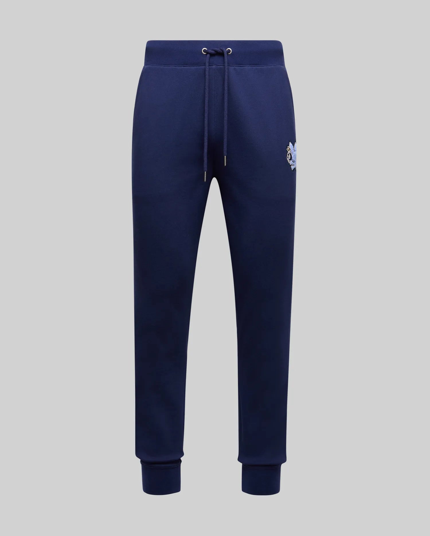The Psycho Bunny MENS AUGUSTE JOGGER - MB0800015 in navy blue is crafted from 100% cotton with a drawstring waist, side pockets, ribbed cuffs, and a small embroidered tiger logo on the left hip, shown on a plain light grey background.