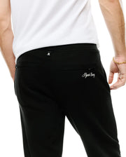 Men's Jacques Pique Track Pants in black, featuring a subtle pique texture, relaxed fit, a small white Psycho Bunny skull logo tag on the waistband, and white embroidered Psycho Bunny script on the back right pocket. (3)