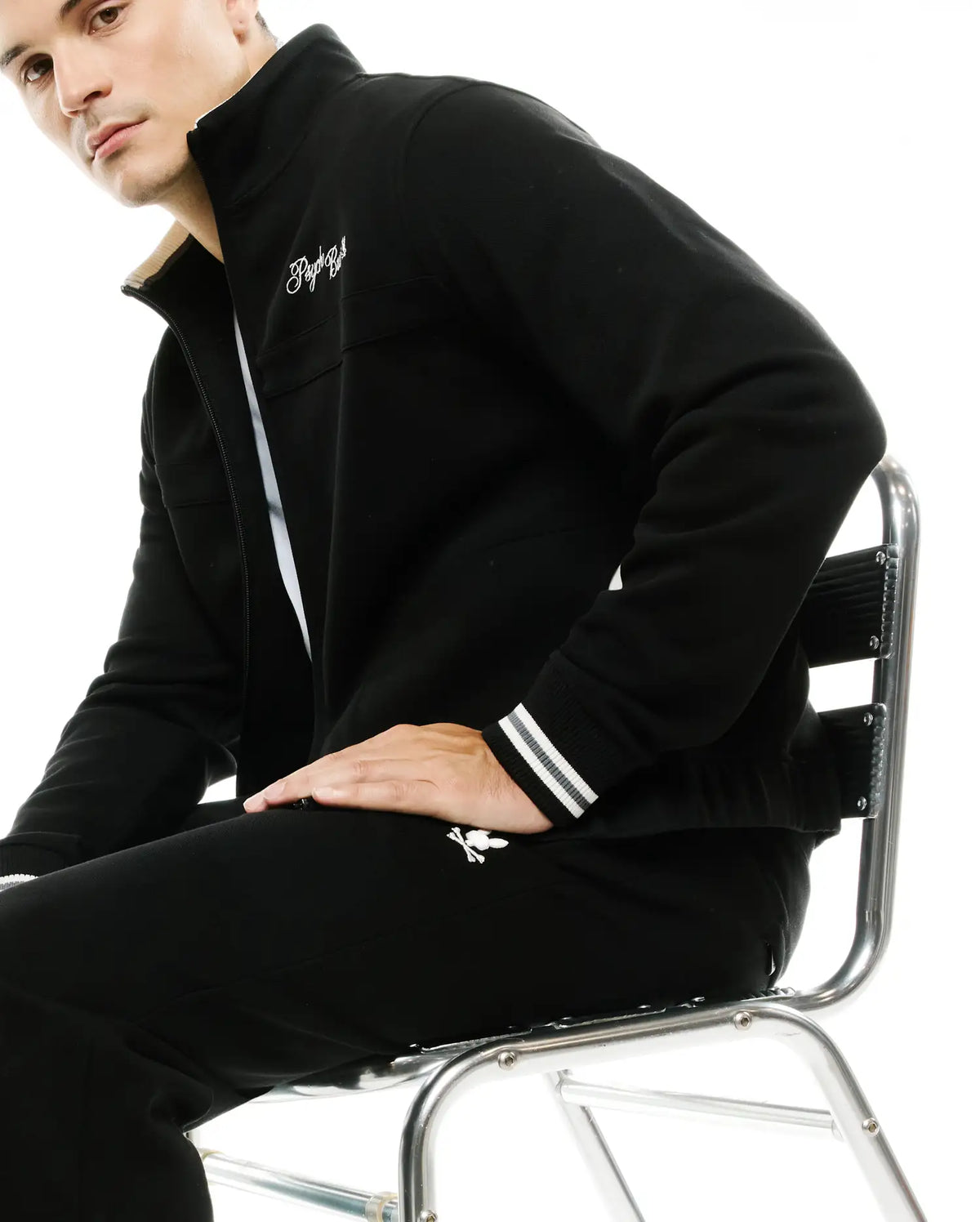Black full-zip track jacket with cream collar lining, white embroidered script logo, striped cuffs, and matching Men's Jacques Pique Track Pants with white bunny skull logo. (4)
