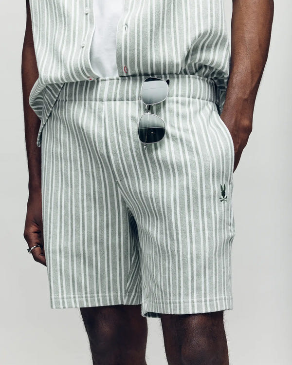 A person wearing Psycho Bunny’s MENS ROBERT KNIT STRIPE SHORT - MB0900007 in light gray and white stripes, with sunglasses hooked on the waistband and one hand in their pocket. Only the lower torso and upper legs are visible.