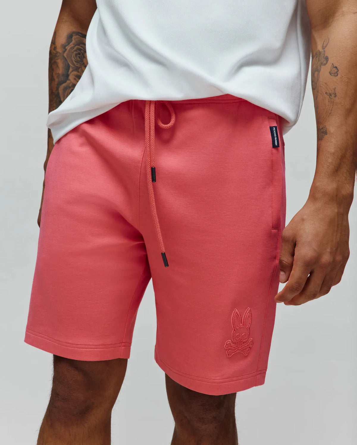 Mens Barry Short, coral relaxed fit French terry shorts with black-tipped drawstring, embroidered Psycho Bunny skull logo on left leg, and side seam brand tag.