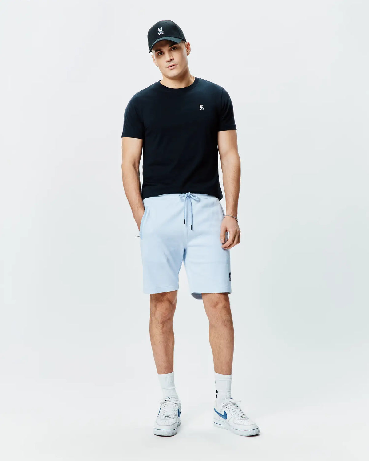 Black jersey t-shirt with white Psycho Bunny logo on chest, light blue Mens Keith Short 8 French terry shorts with black drawstrings and bunny logo on thigh, plus a black cap with white bunny skull. (4)