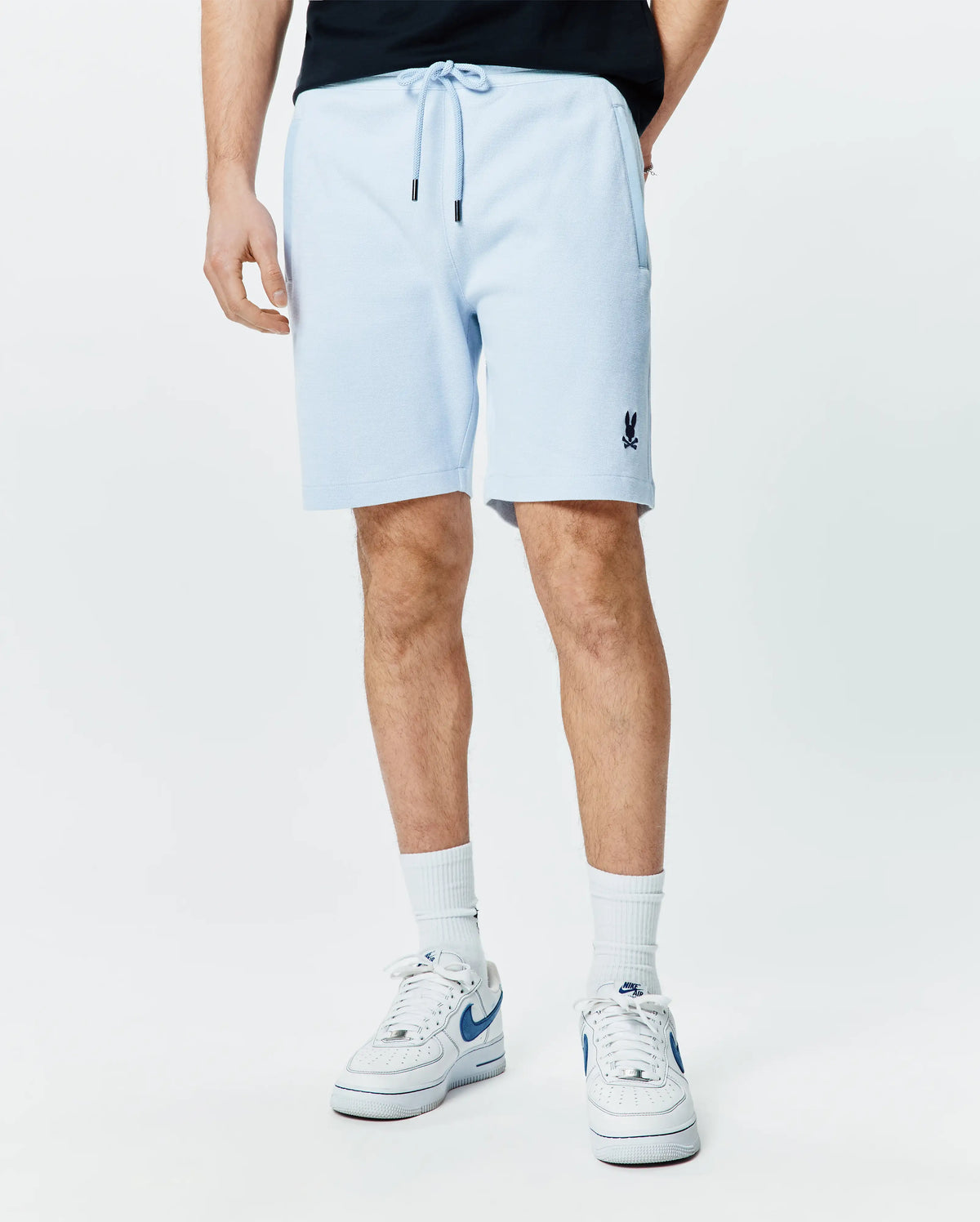 Mens Keith Short 8 light blue pique knit shorts, relaxed fit, featuring a drawstring waist with black tips, side pockets, and a small embroidered navy Psycho Bunny skull logo on the left leg. (1)