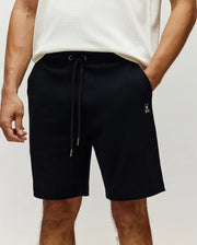 Black Mens Maxton Waffle Sweatshort in a relaxed fit, featuring a waffle knit texture, drawstring waist with silver tips, and a small embroidered white Psycho Bunny skull logo on the left thigh.