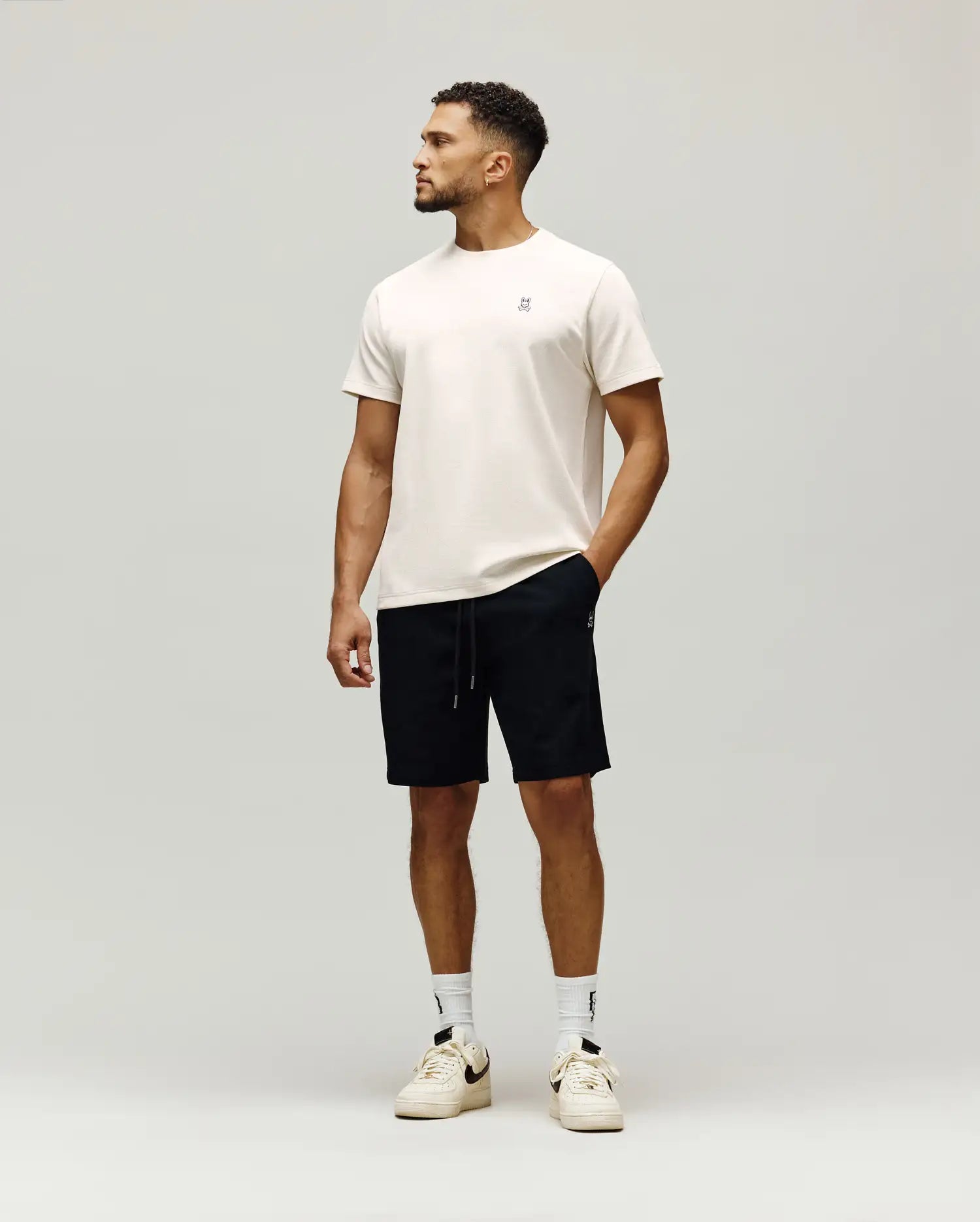 Cream classic fit jersey t-shirt with small embroidered dark Psycho Bunny skull logo on left chest, paired with black MENS MAXTON WAFFLE SWEATSHORT featuring a drawstring waist and small white Psycho Bunny logo on left thigh.