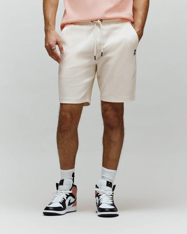 MENS MAXTON WAFFLE SWEATSHORT in cream, featuring a relaxed fit, waffle knit texture, drawstring waist, and a small embroidered black Psycho Bunny skull logo on the left thigh.