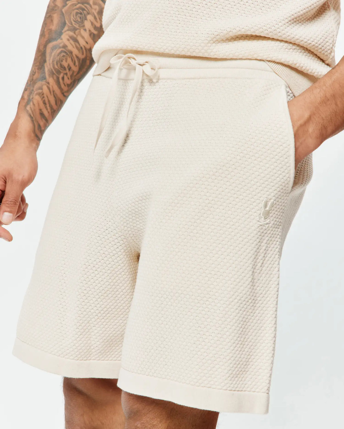 Mens Devon Knit Short, cream textured knit shorts with a relaxed fit, drawstring waist, and small tonal embroidered Psycho Bunny skull logo on the left thigh. (2)