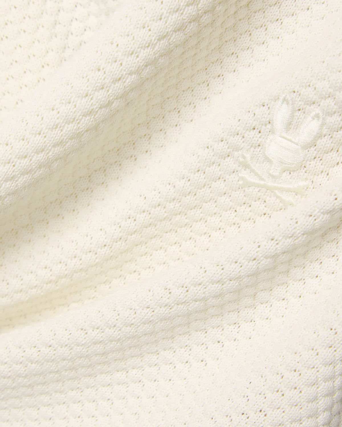Mens Devon Knit Short in premium cream, featuring a soft, subtly patterned open knit fabric and a small, tone-on-tone embroidered Psycho Bunny skull logo detail. (6)